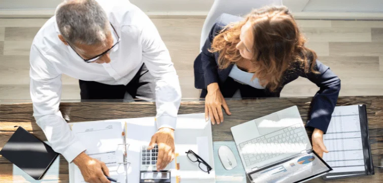 Two people at a desk with lots of documents