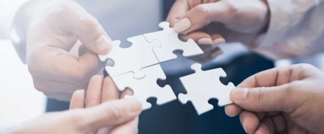 Vier Personen halten jeweils ein großes weißes Puzzleteil aneinander