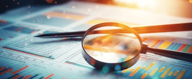 Lupe und Stift liegen auf Dokumenten mit Diagrammen