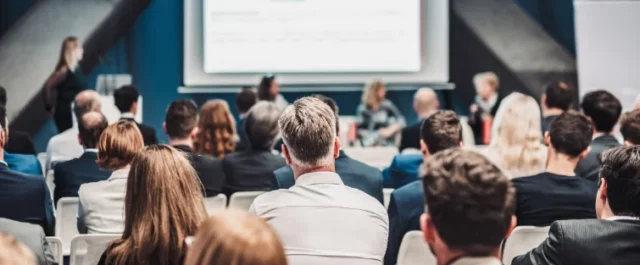 Menschen sitzen in Rückansicht vor Präsentation