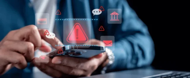 Mann mit Laptop und Handy umgeben von roten Ausrufezeichen