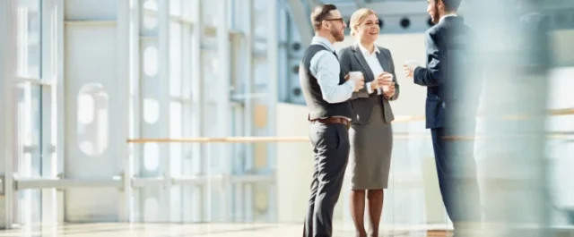 Drei Personen in Businesskleidung unterhalten sich im Flur eines modernen Büros