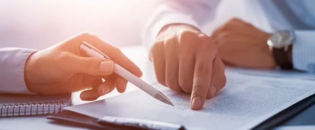 zwei Hände zeigen auf Dokument mit Stift