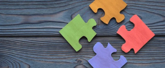 vier verschiedenfarbige Puzzleteile auf Holz